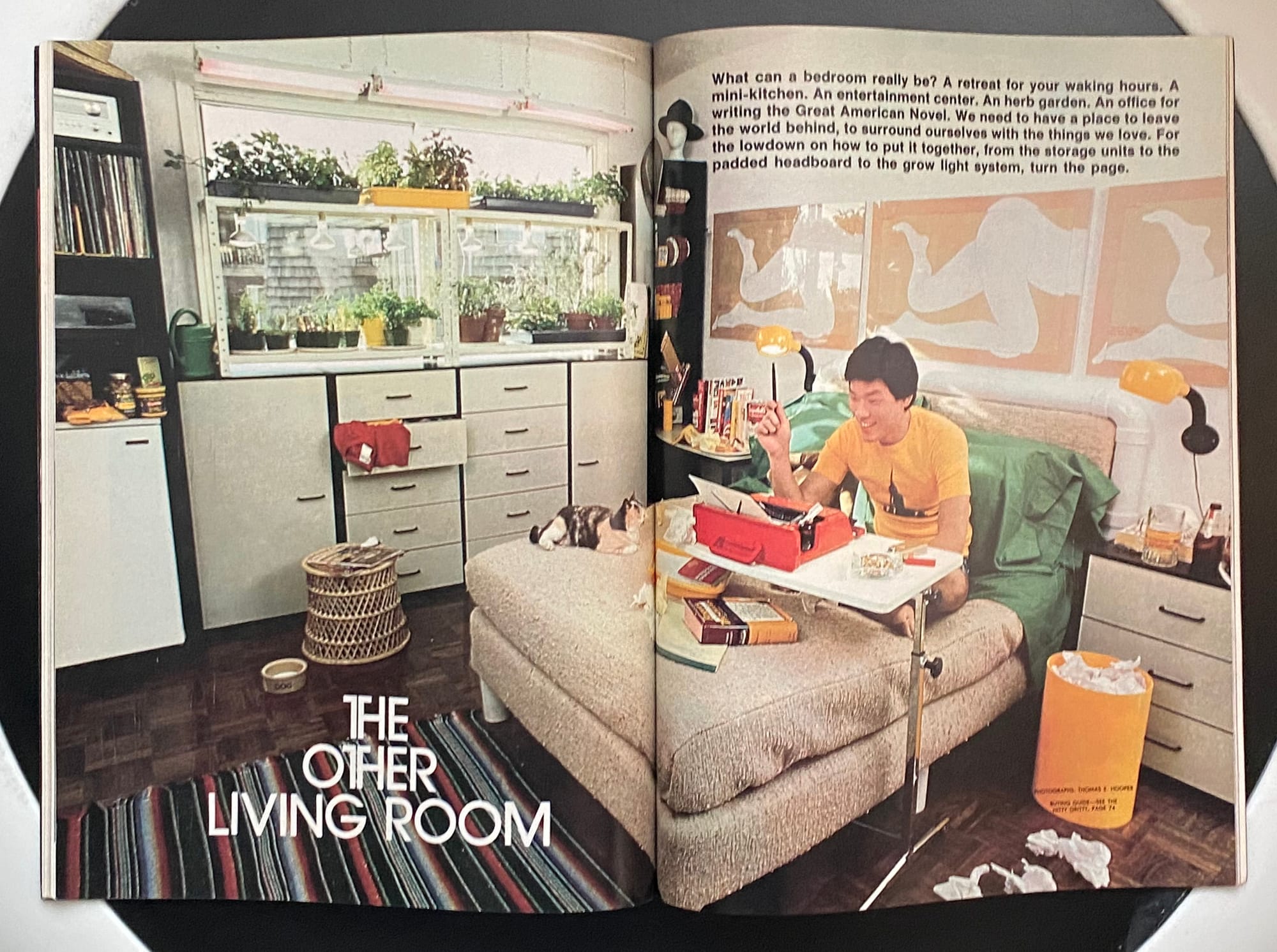 A guy working from his bed with a bright red typewriter on a cantilevered table.