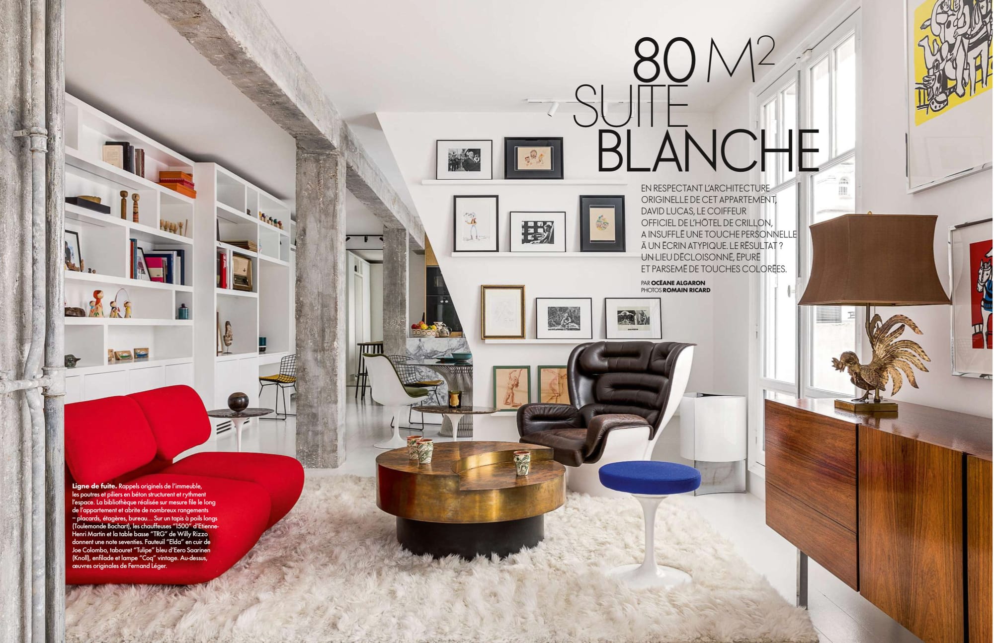 Apartment with white walls and floor and very little colour, except a red sofa, blue stool cushion, and yellow background in a print.