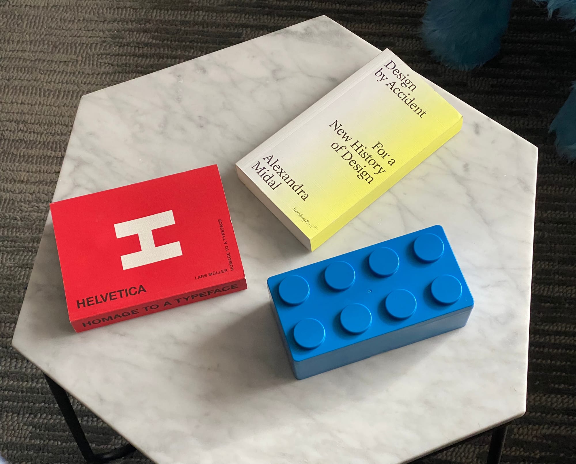 Red book on Helvetica, blue Lego-block-styled box, and mostly yellow book, all on a marble tabletop.