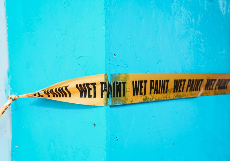 Turquoise wall with Wet Paint ribbon stretched across it.