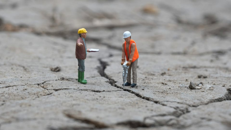 Two construction worker figurines, one with a jackhammer, the other with a clipboard.