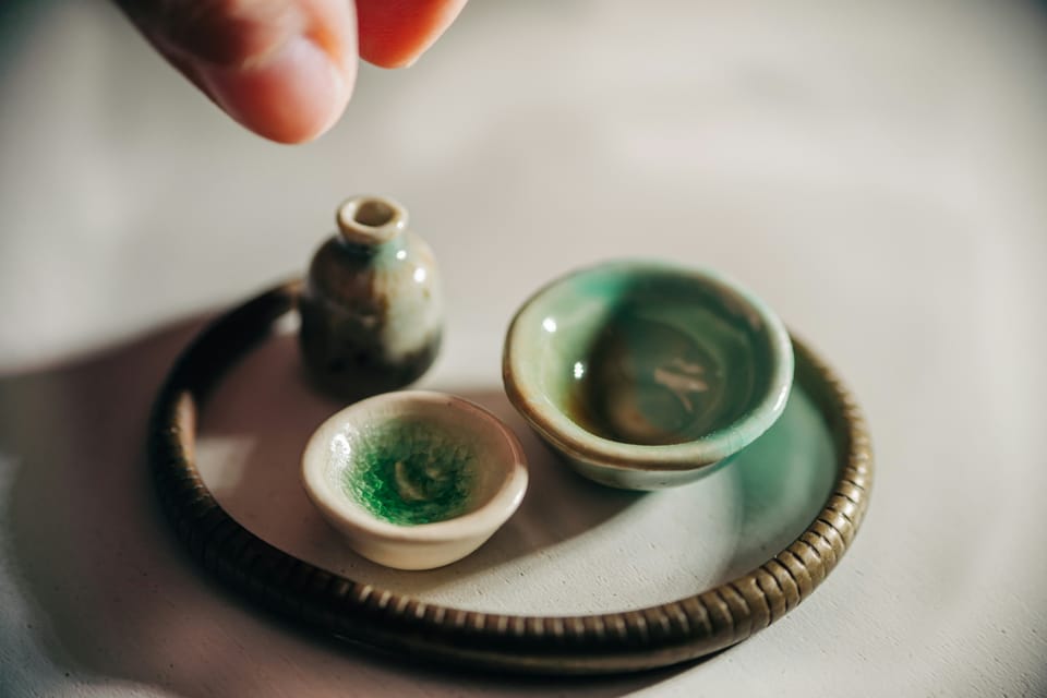Tiny ceramic objects with a large thumb and forefinger above, as if it's about to pick an object up.